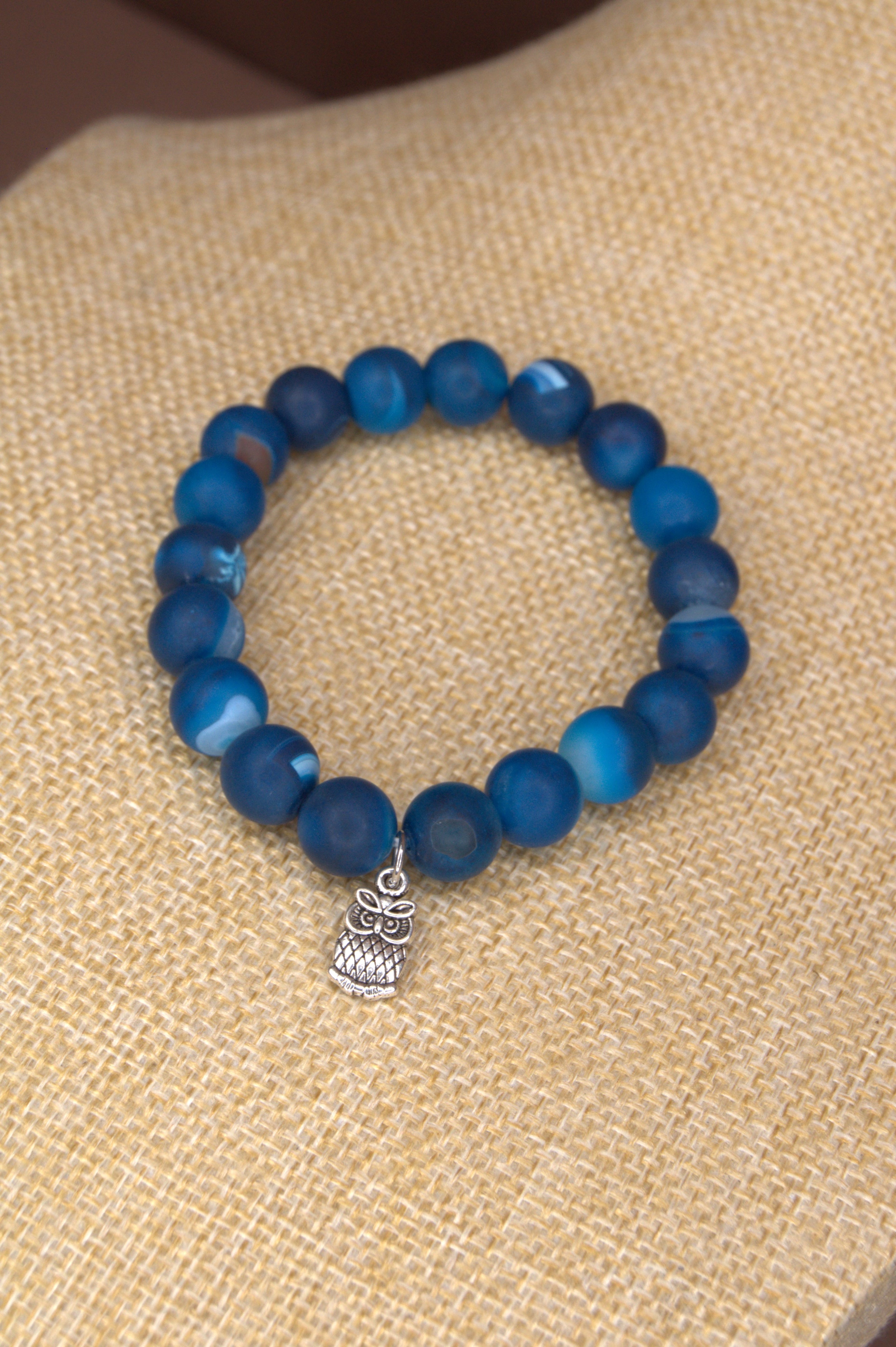 Blue beaded bracelet with a silver owl charm on a beige fabric background