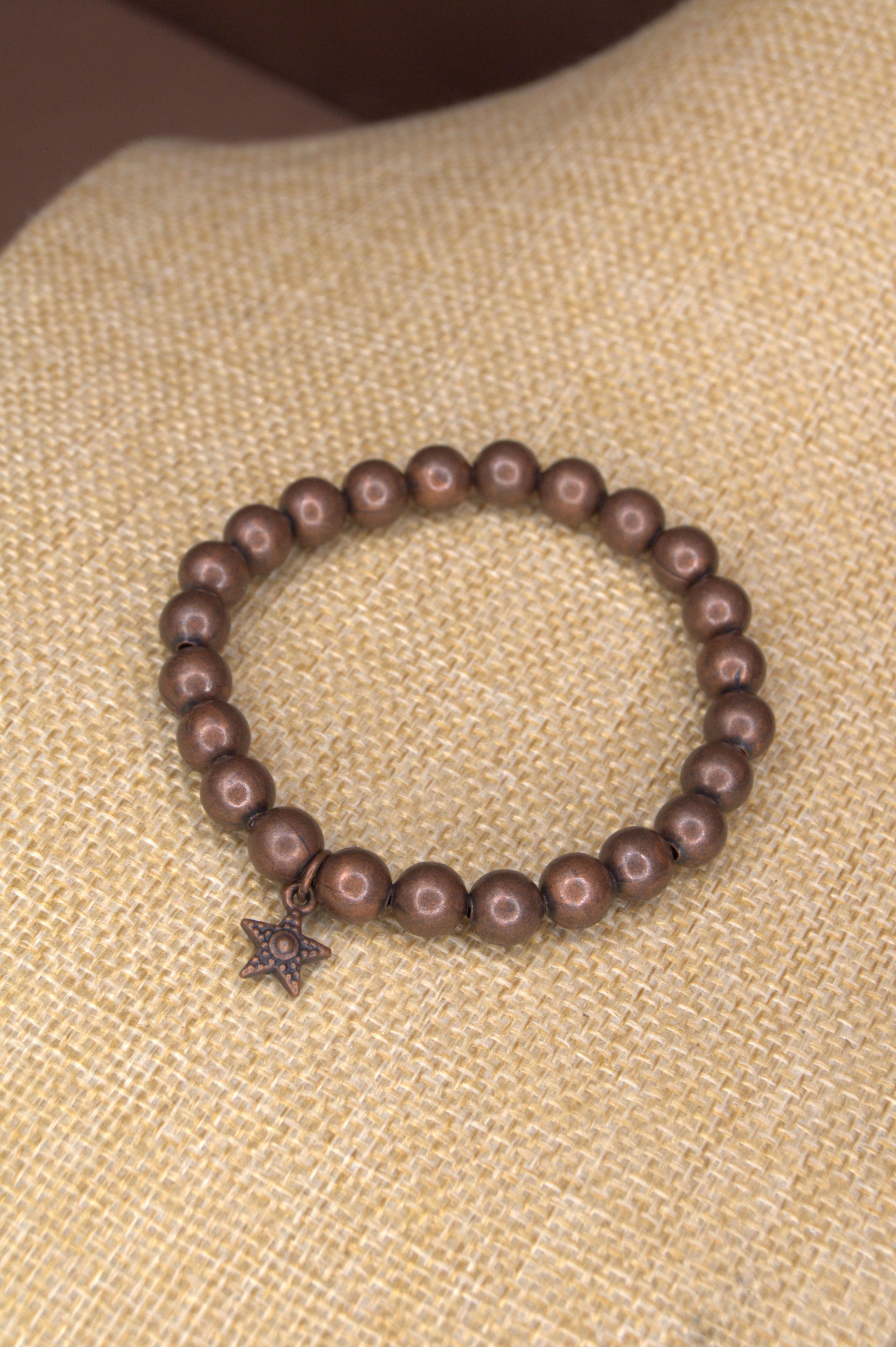 Copper metal beaded bracelet with a star charm on a textured beige background