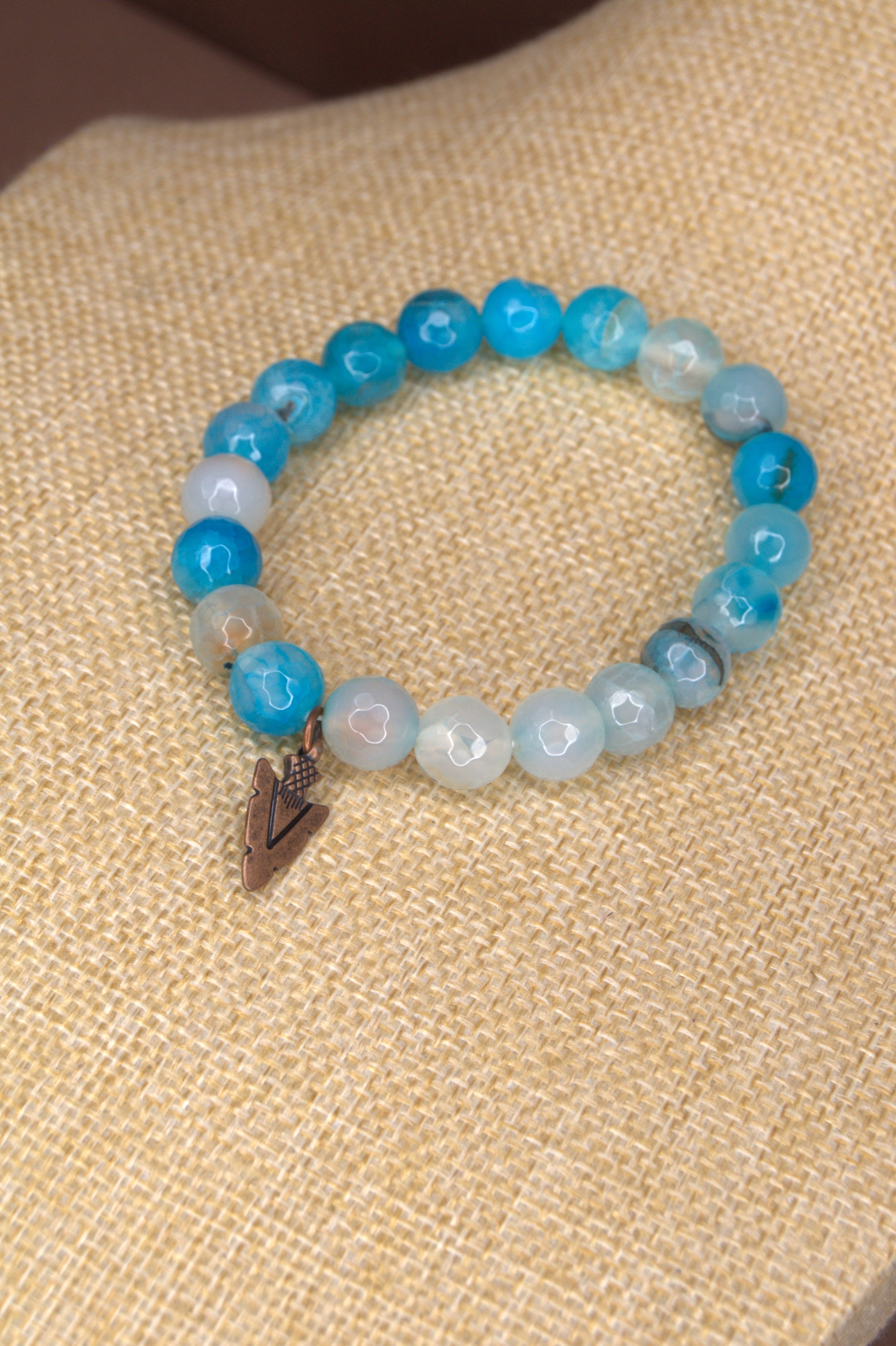 Beaded bracelet with blue and white beads  and copper arrowhead charm on a textured beige surface