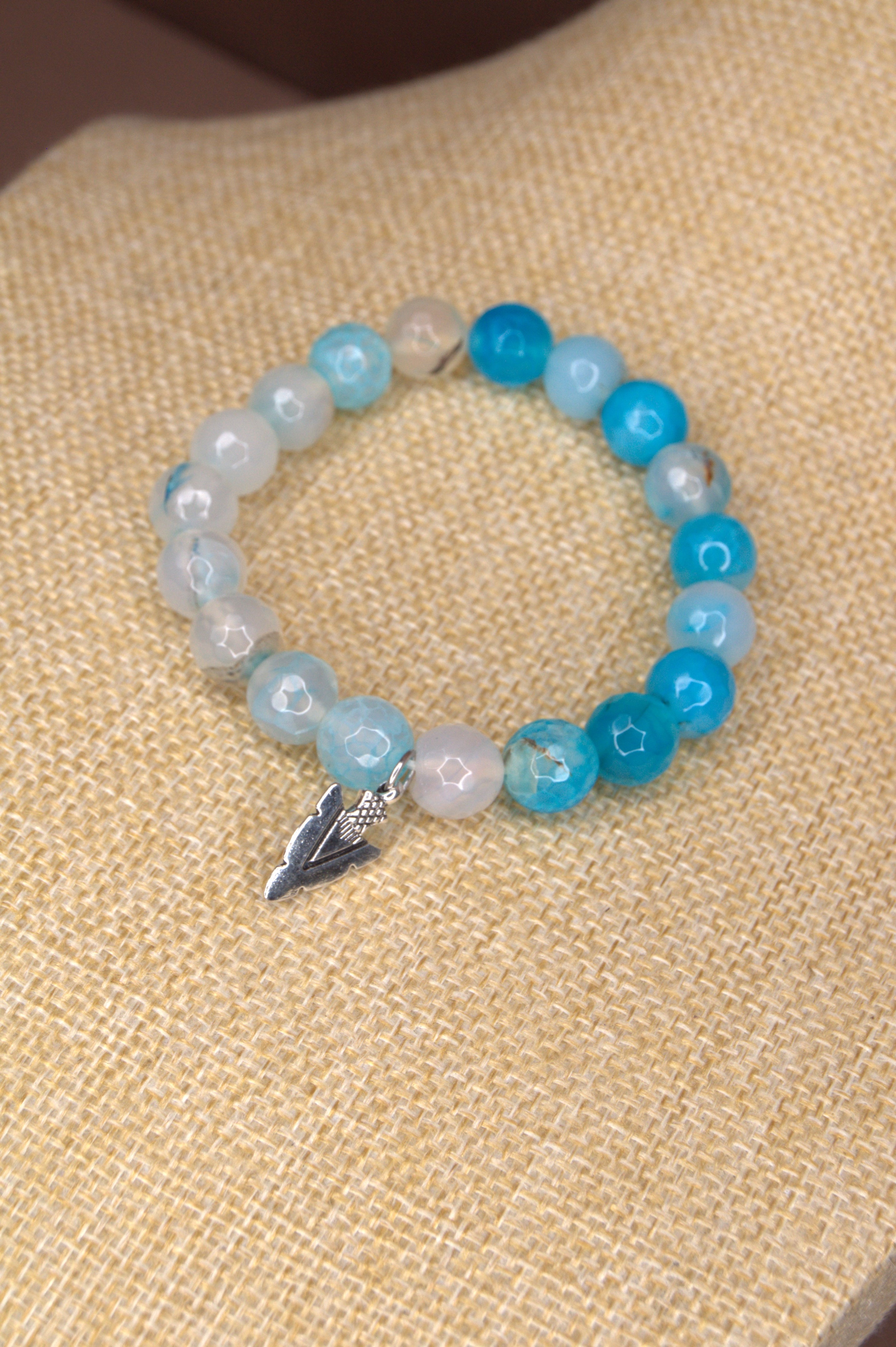 Beaded bracelet with blue and white beads  and silver arrowhead charm on a textured beige surface