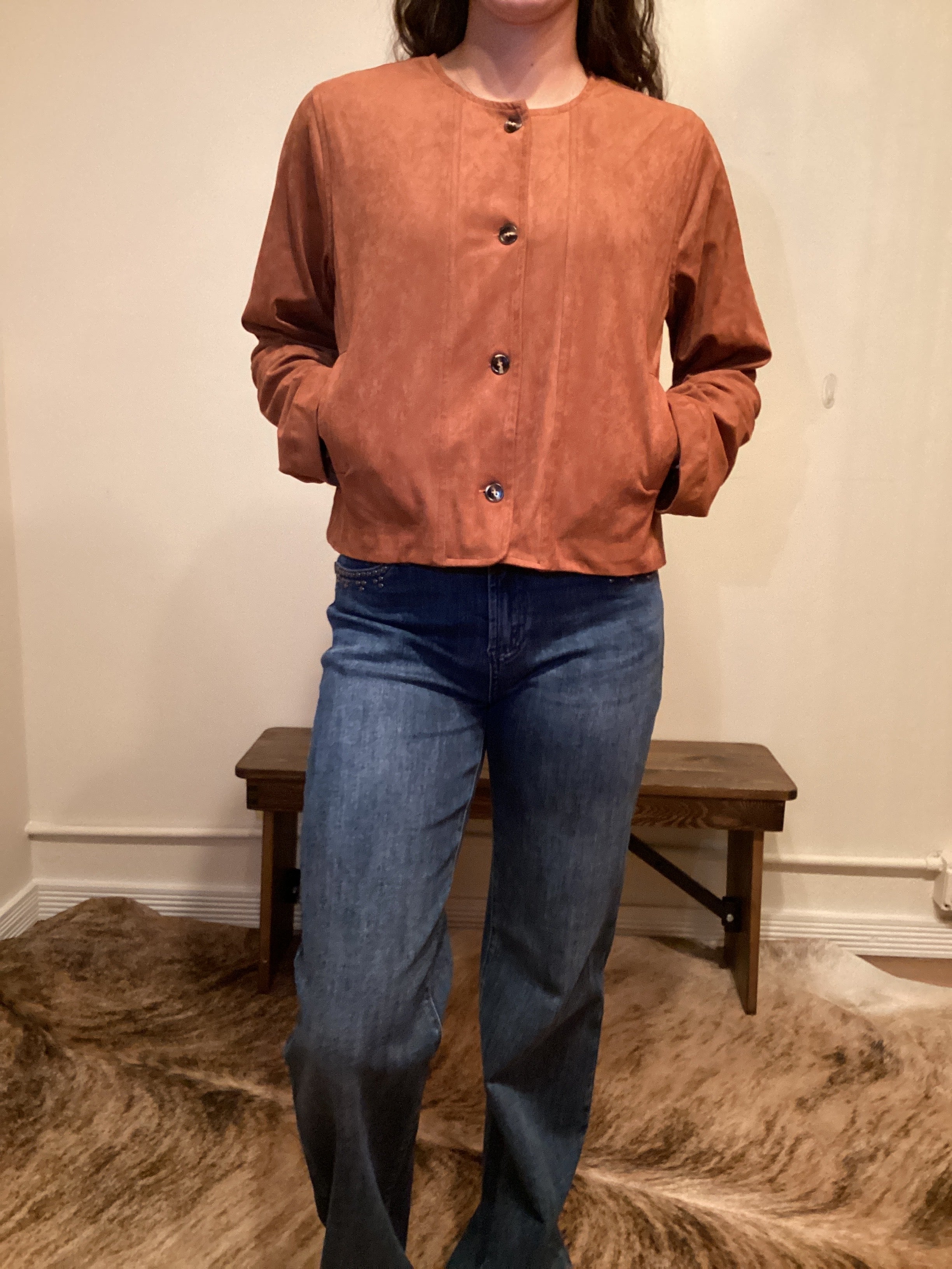 Person wearing a brown faux leather button up jacket and blue jeans 