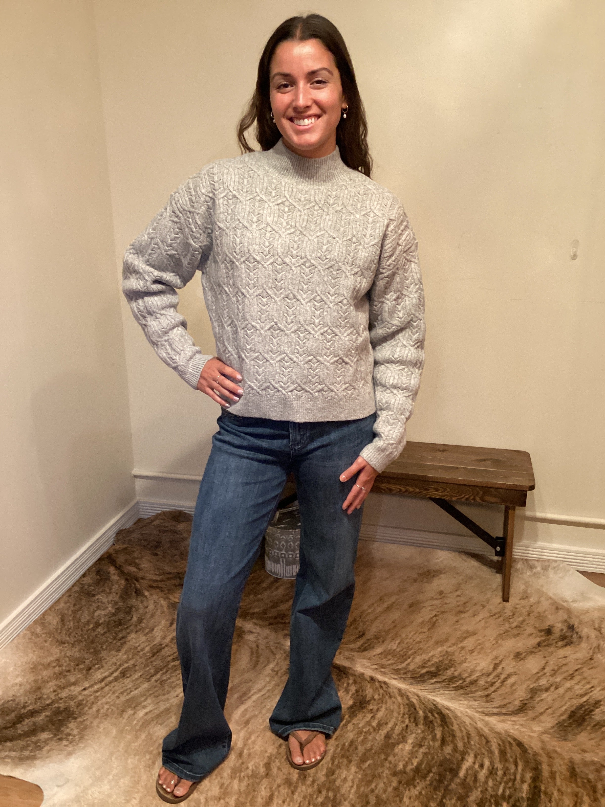 Person wearing a gray sweater and blue jeans standing on a carpeted floor.