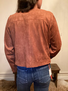 Back View Person wearing a brown faux leather button up jacket and blue jeans 