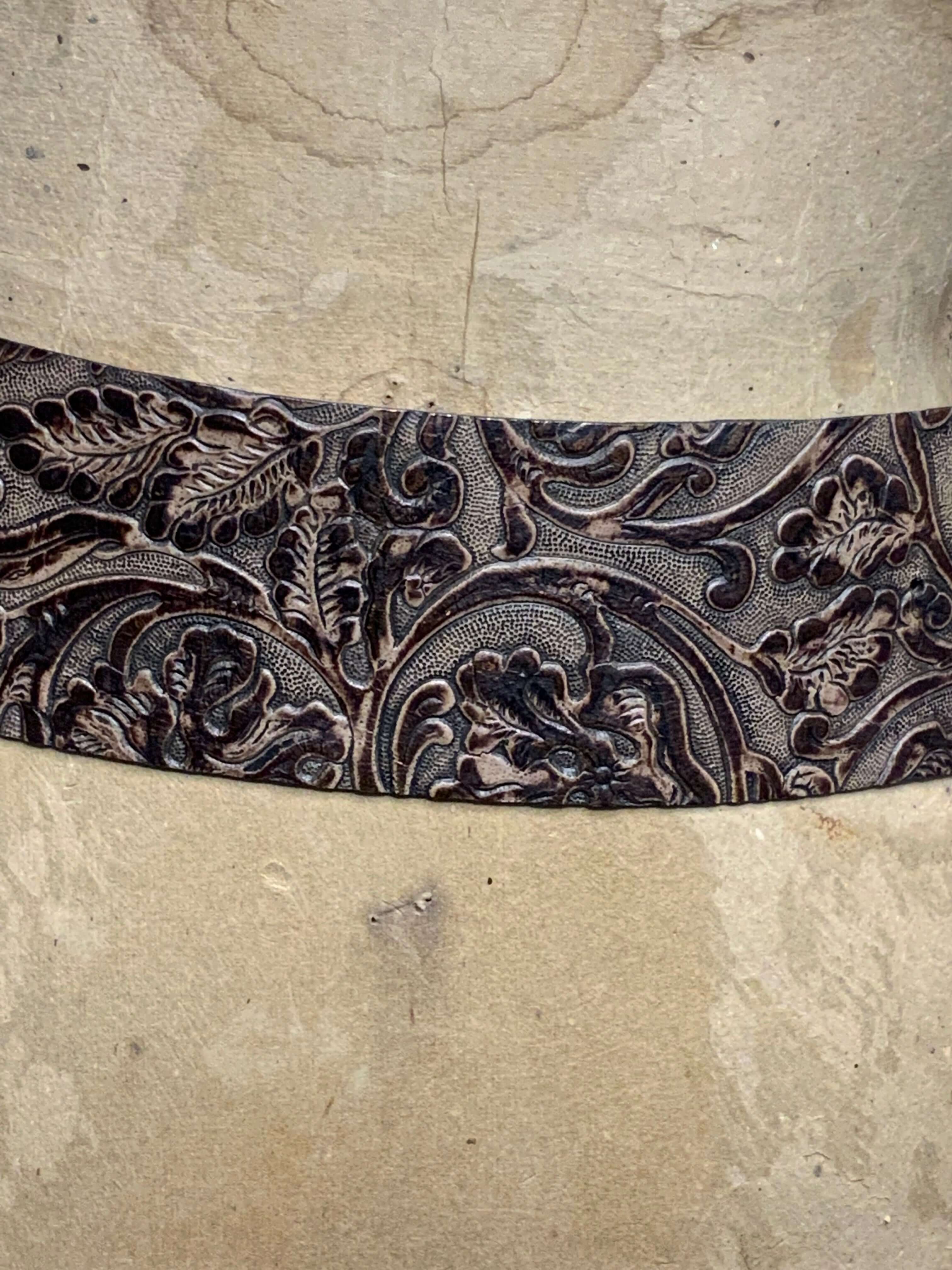 Decorative leather belt with intricate floral patterns on a textured beige background