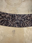 Decorative leather belt with intricate floral patterns on a textured beige background