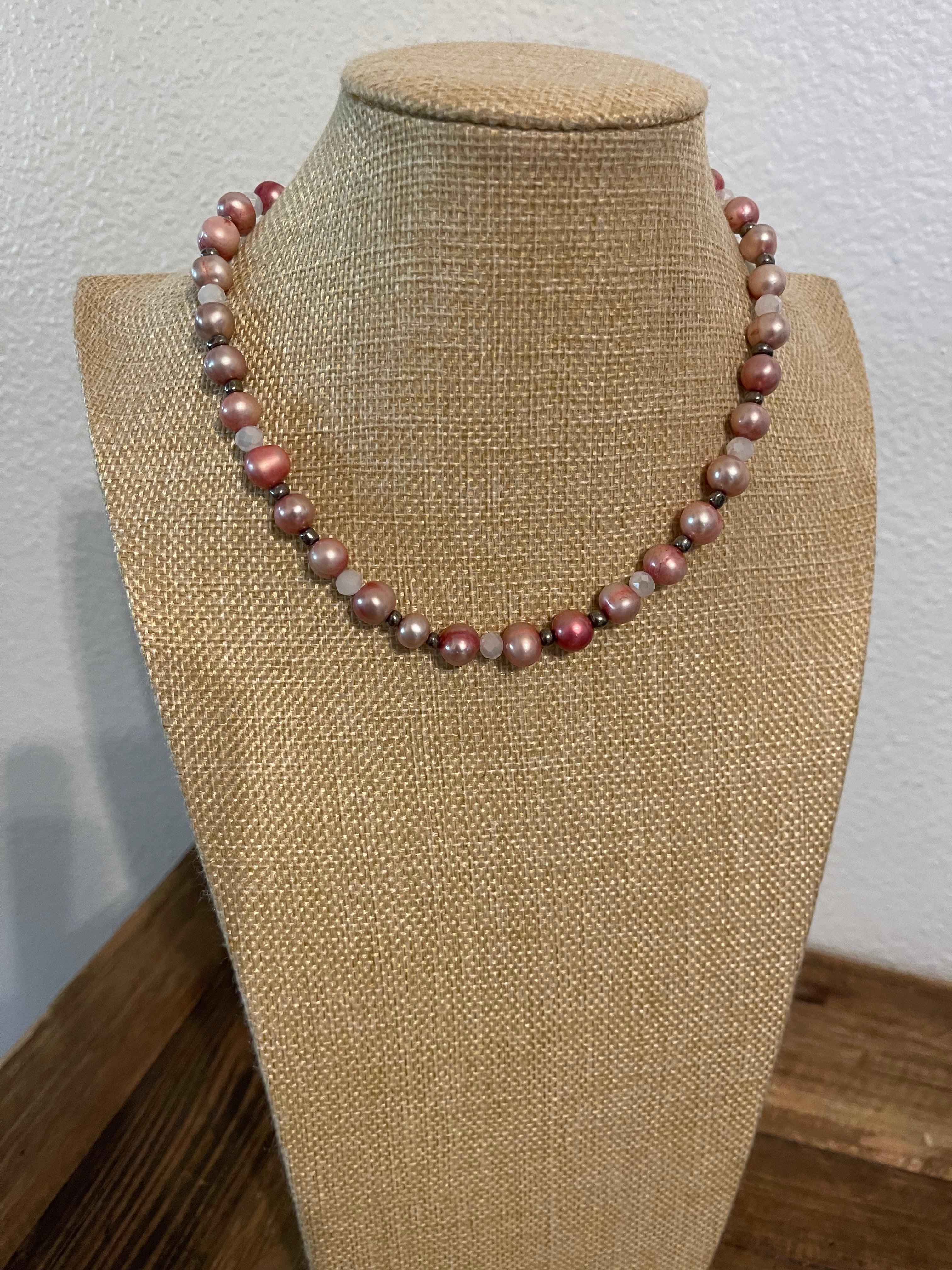 Necklace with pink dyed pearls and white crystals with silver bead accents on a beige mannequin.