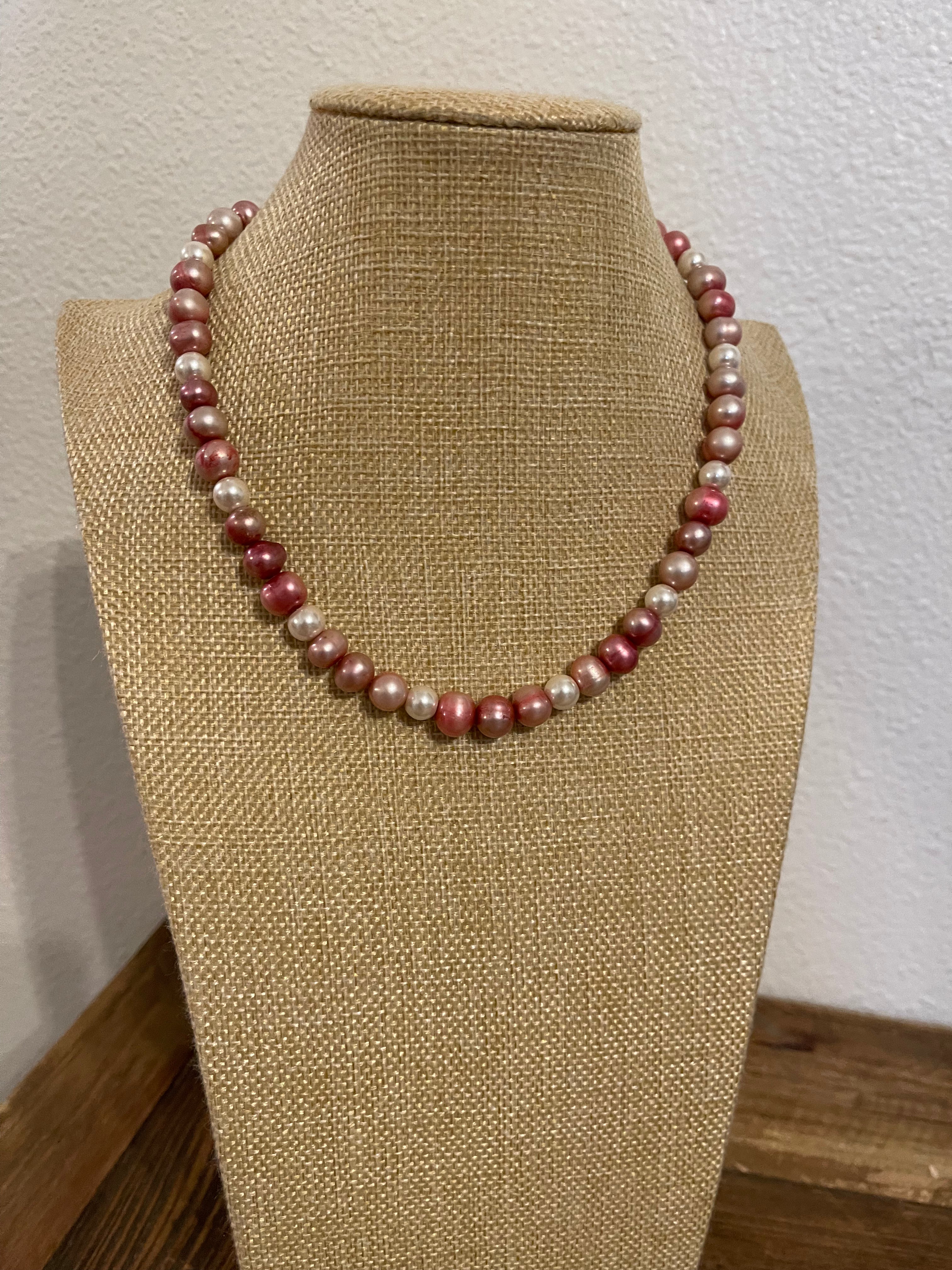 Pink and ivory pearl necklace on a beige mannequin bust against a white wall.