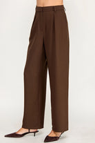 A person wearing high-waisted, wide-leg brown trousers with a matching belt, styled with dark brown pointed-toe slingback heels against a plain light gray studio background.