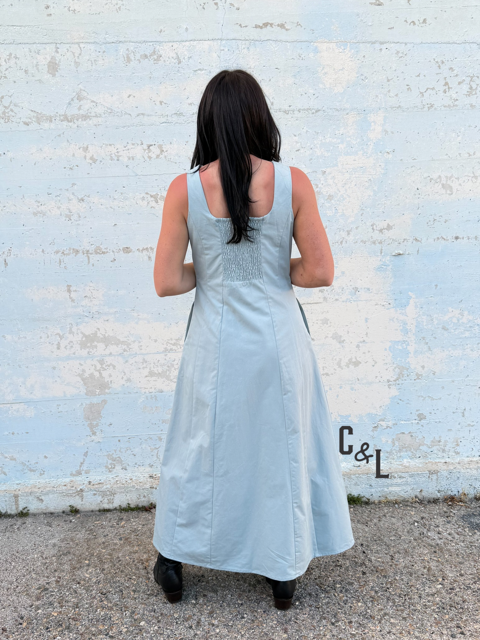 Woman wearing a light blue dress standing against a textured white wall.