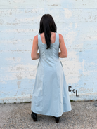 Woman wearing a light blue dress standing against a textured white wall.