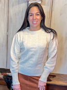 Woman wearing a light sweater and brown skirt standing in a room with wooden furniture.