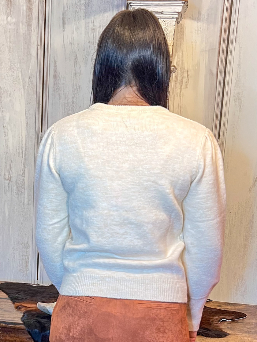 Person wearing a light-colored sweater and brown skirt standing in front of a wooden table.