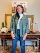 Woman wearing a green jacket and blue jeans standing in front of a table with decorative items.