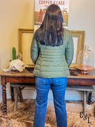 Person wearing a green puffer jacket and blue jeans standing in front of a table with decorative items.