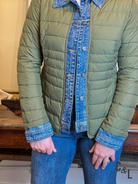 Green quilted jacket with denim collar and cuffs worn by a person indoors.