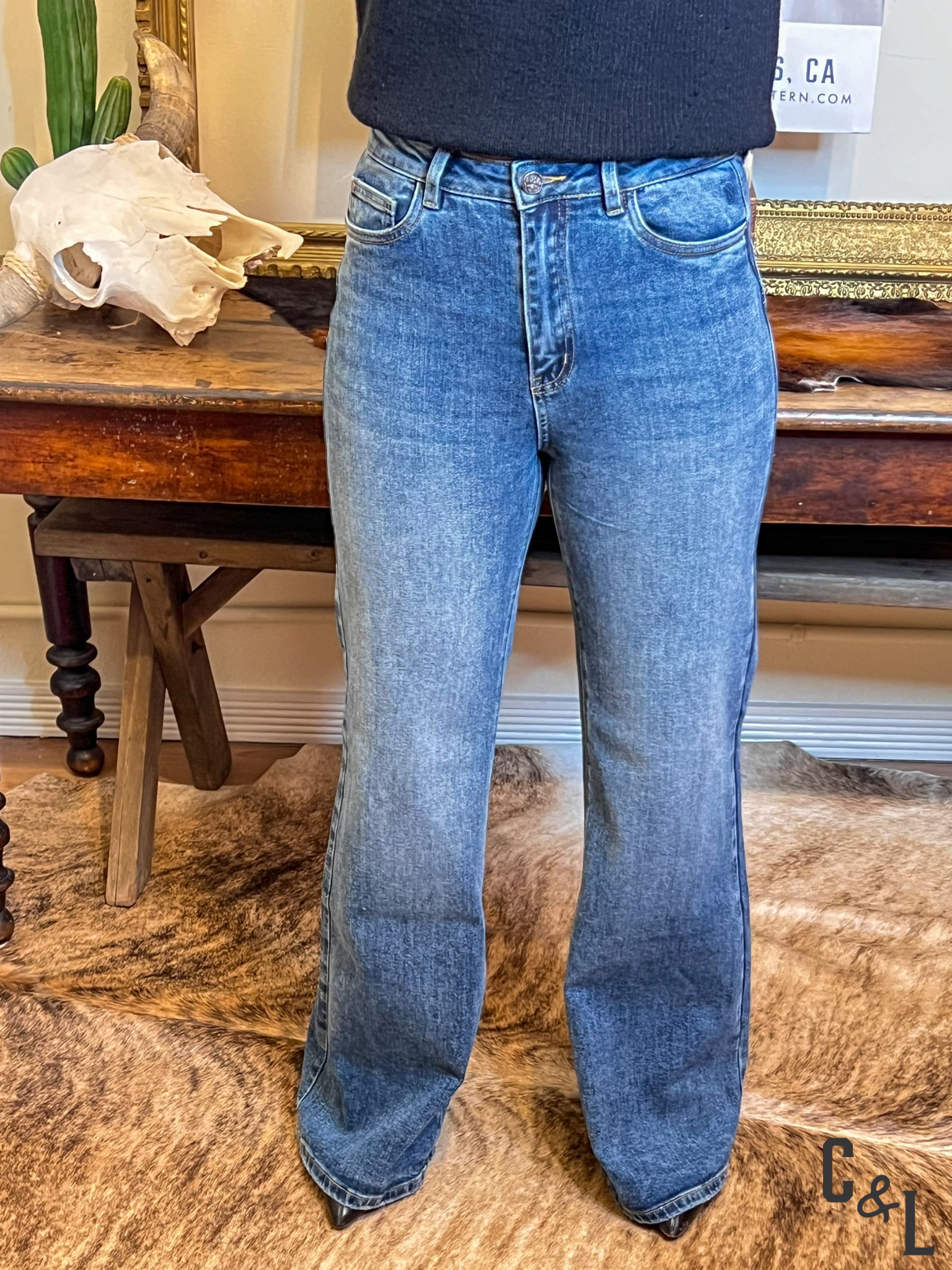 Person wearing blue jeans standing in a room with wooden furniture and decor.