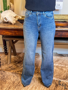 Person wearing blue jeans standing in a room with wooden furniture and decor.