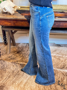 Person wearing blue jeans standing on a wooden floor with a rustic background