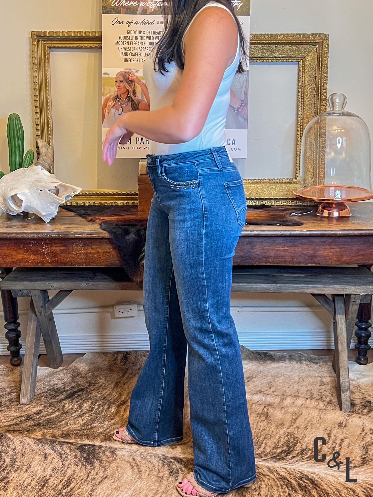 Person wearing blue jeans standing in a room with a wooden table and decorative items.