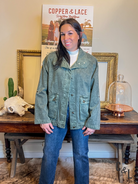Woman wearing a green jacket and blue jeans standing in front of a 'Copper & Lace' sign.