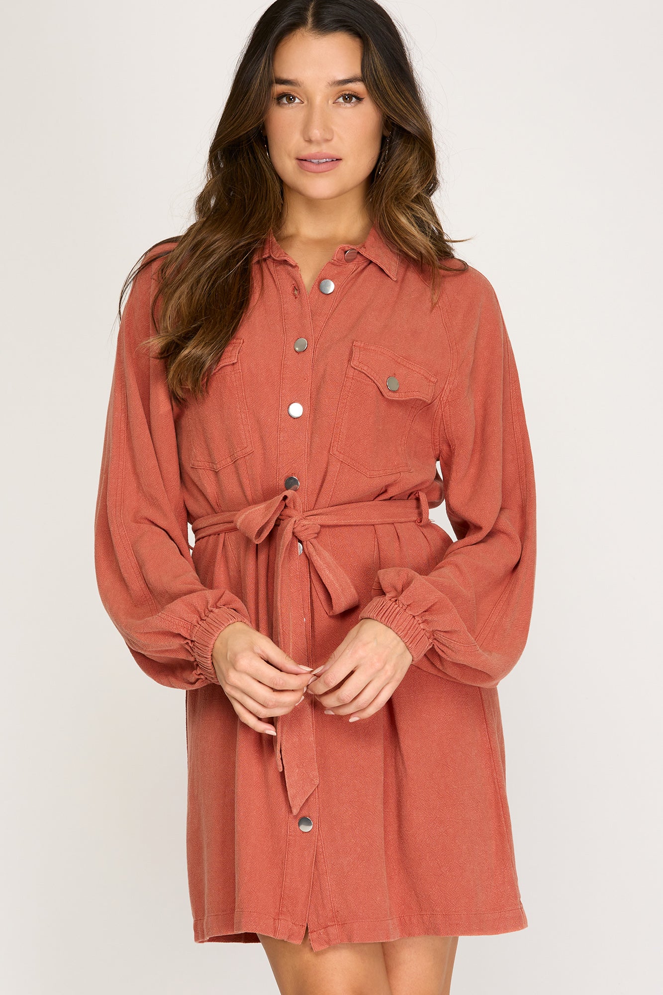 Woman wearing a light rust long sleeve button up  dress against a white background