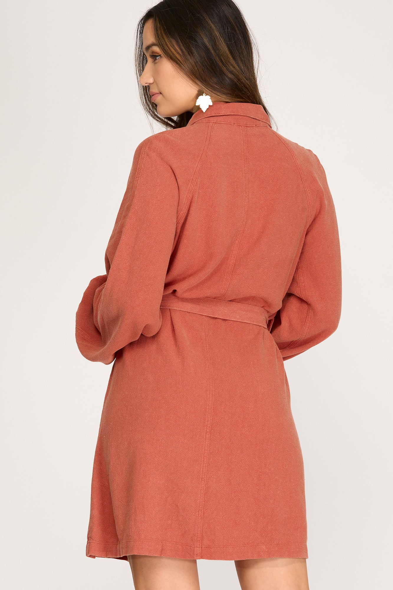 Woman wearing a light rust long sleeve button up  dress against a white background
