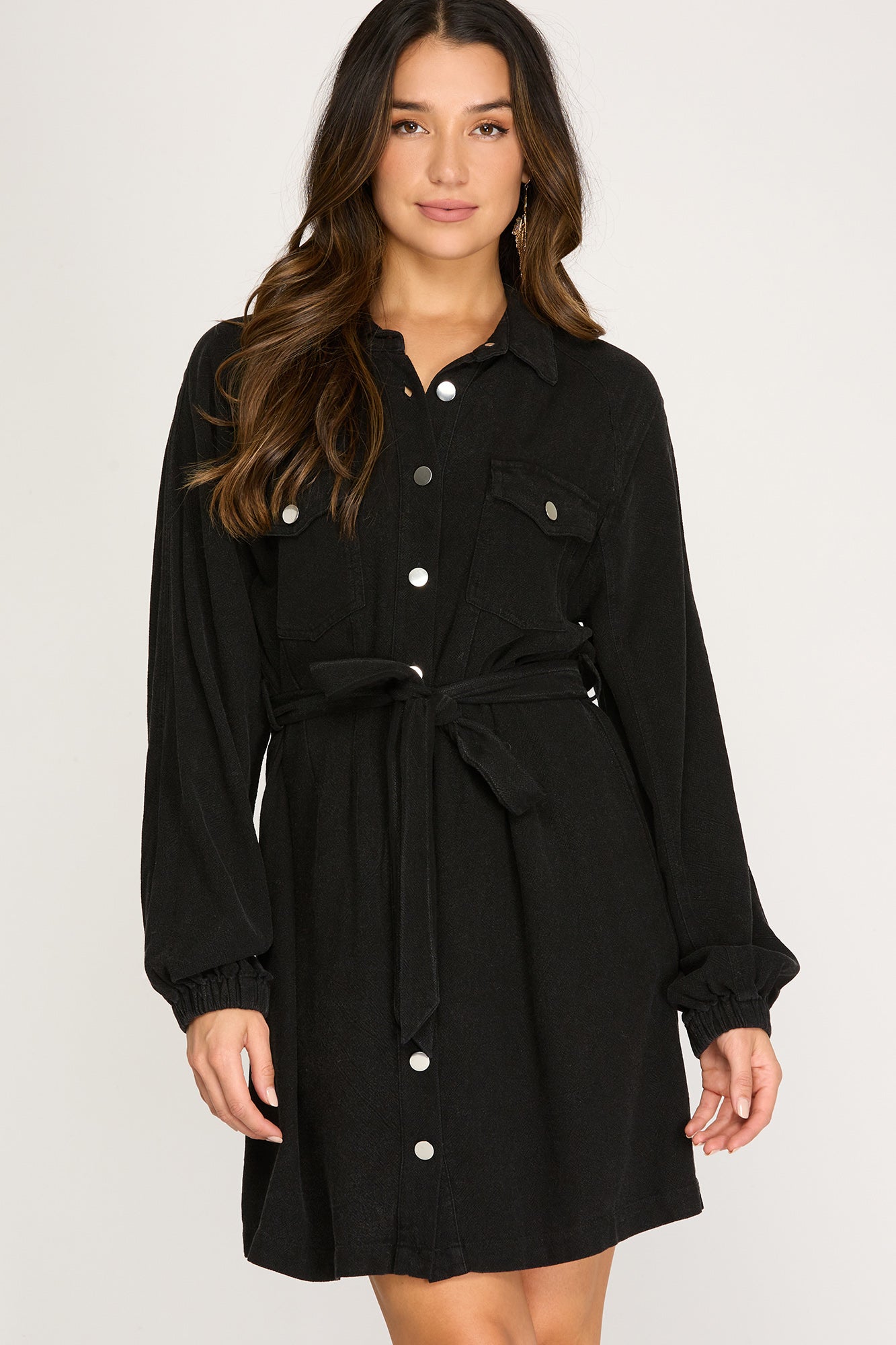 Woman wearing a black long sleeve button up  dress against a white background