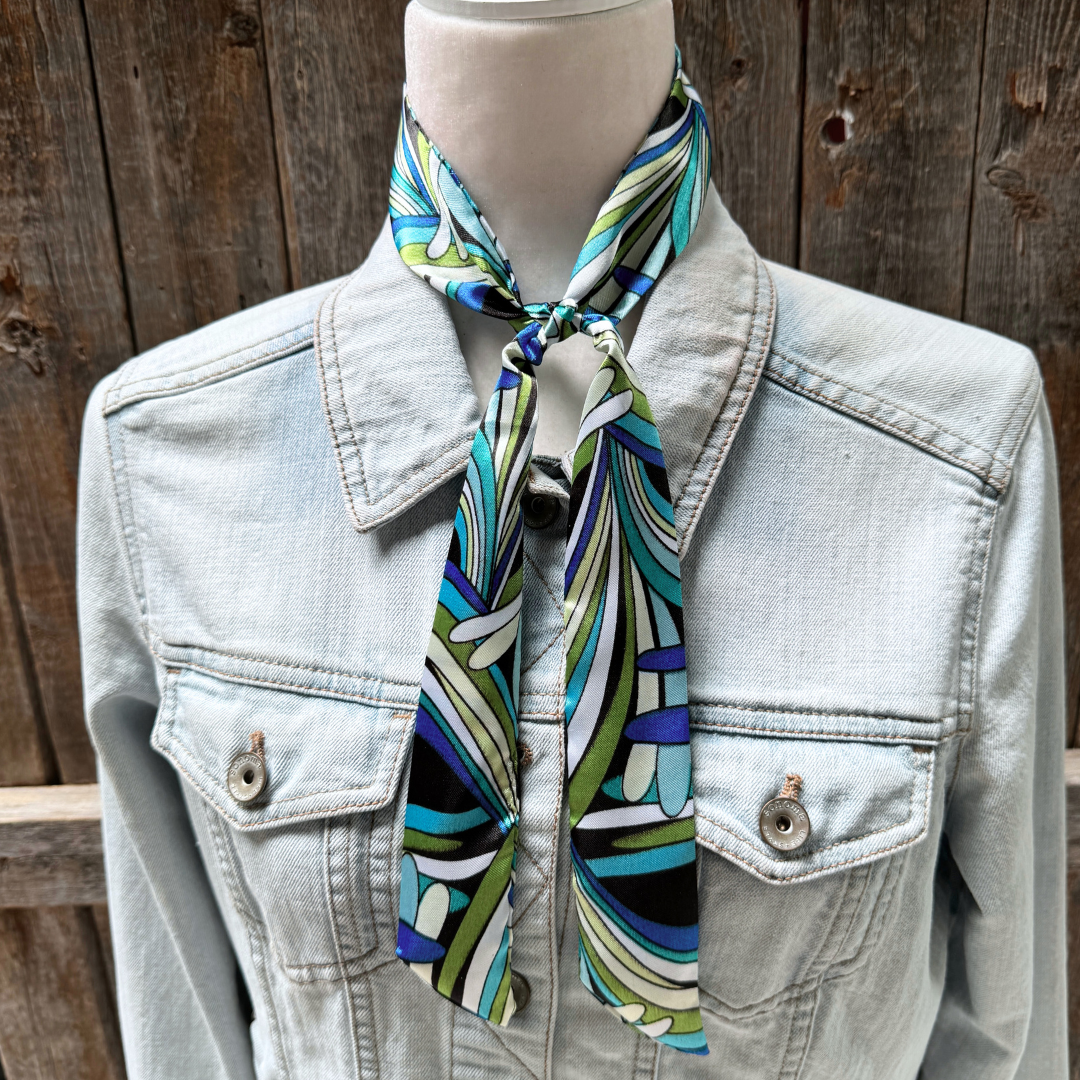 Mannequin wearing a light blue denim jacket with a colorful patterned scarf around its neck against a wooden background.