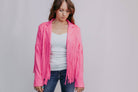 Woman wearing a pink fringed jacket over a white top and blue jeans on a plain background