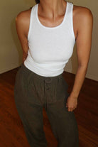 Person wearing a white tank top and brown wide leg pants on a wooden floor.