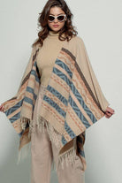 Woman wearing a beige poncho with a  Tan background and light blue, brown, light rust, and grey aztec pattern design  in stripes with tassel trim along bottom hem. Light weight fabric 