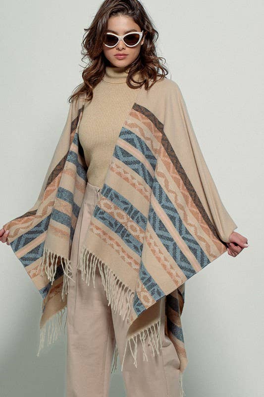 Woman wearing a beige poncho with a  Tan background and light blue, brown, light rust, and grey aztec pattern design  in stripes with tassel trim along bottom hem. Light weight fabric 