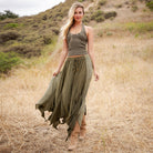A woman stands in a dry grassy field wearing an olive green halter top and a matching olive green maxi skirt with a drawstring waist, paired with brown boots.
