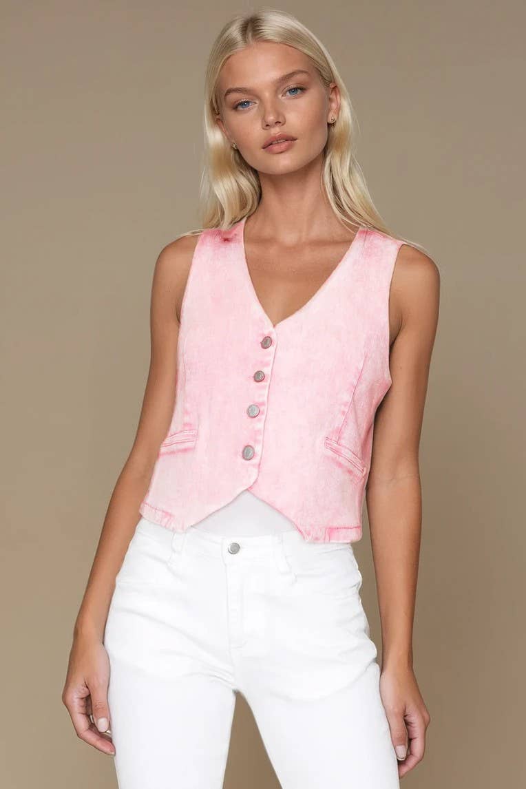 Woman wearing a pink sleeveless top with buttons and white pants on a beige background