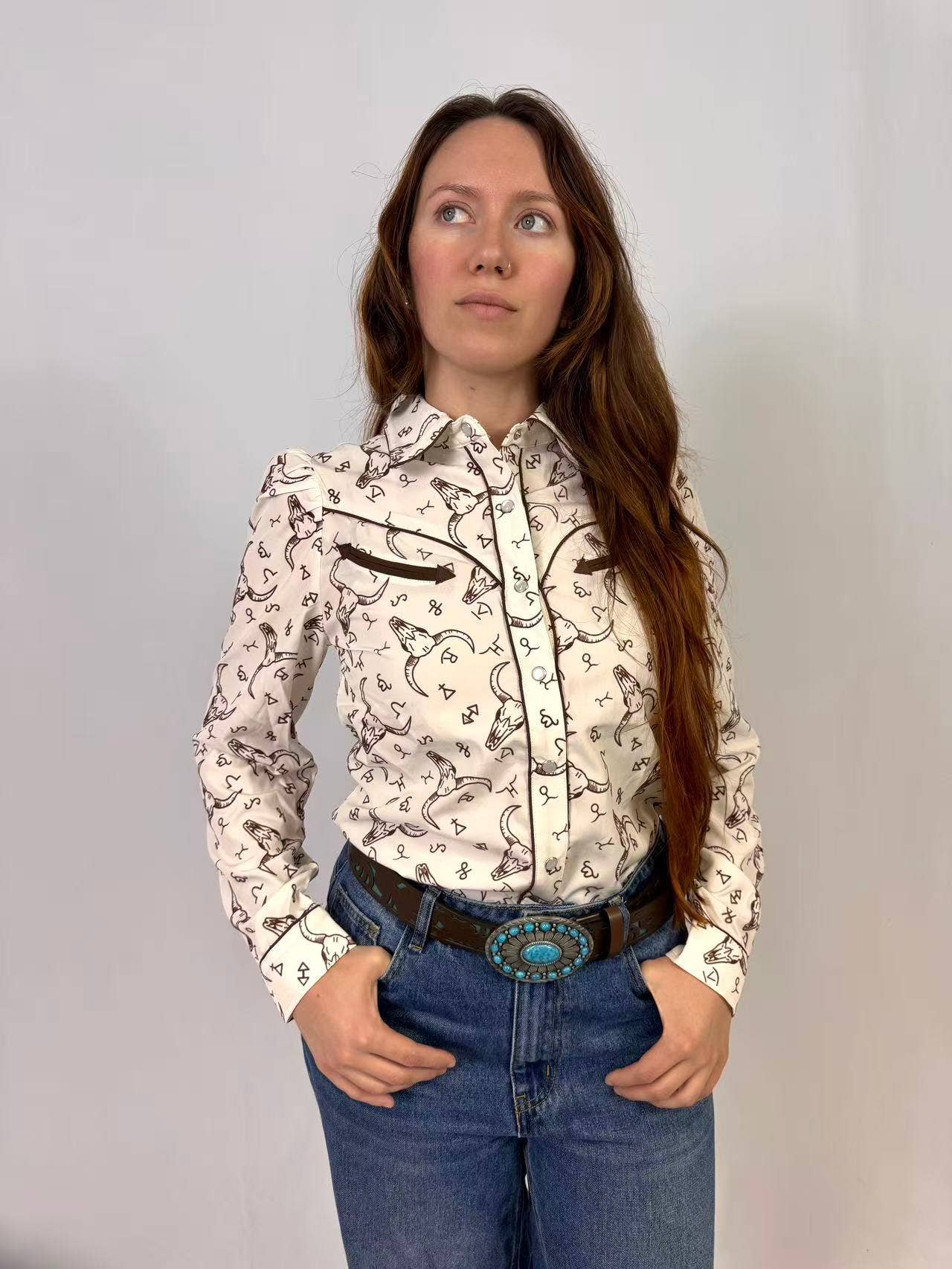 Woman wearing a black and white western print patterned blouse and blue jeans against a plain background