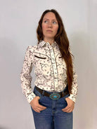 Woman wearing a black and white western print patterned blouse and blue jeans against a plain background