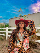 Woman in a leopard print jacket and red hat holding sunflowers against a blue sky.