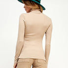Woman wearing a beige long-sleeve top and pants with a green hat on a white background