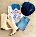 White boots, white t-shirt with graphic design, blue denim shorts, blue hat on a wooden surface