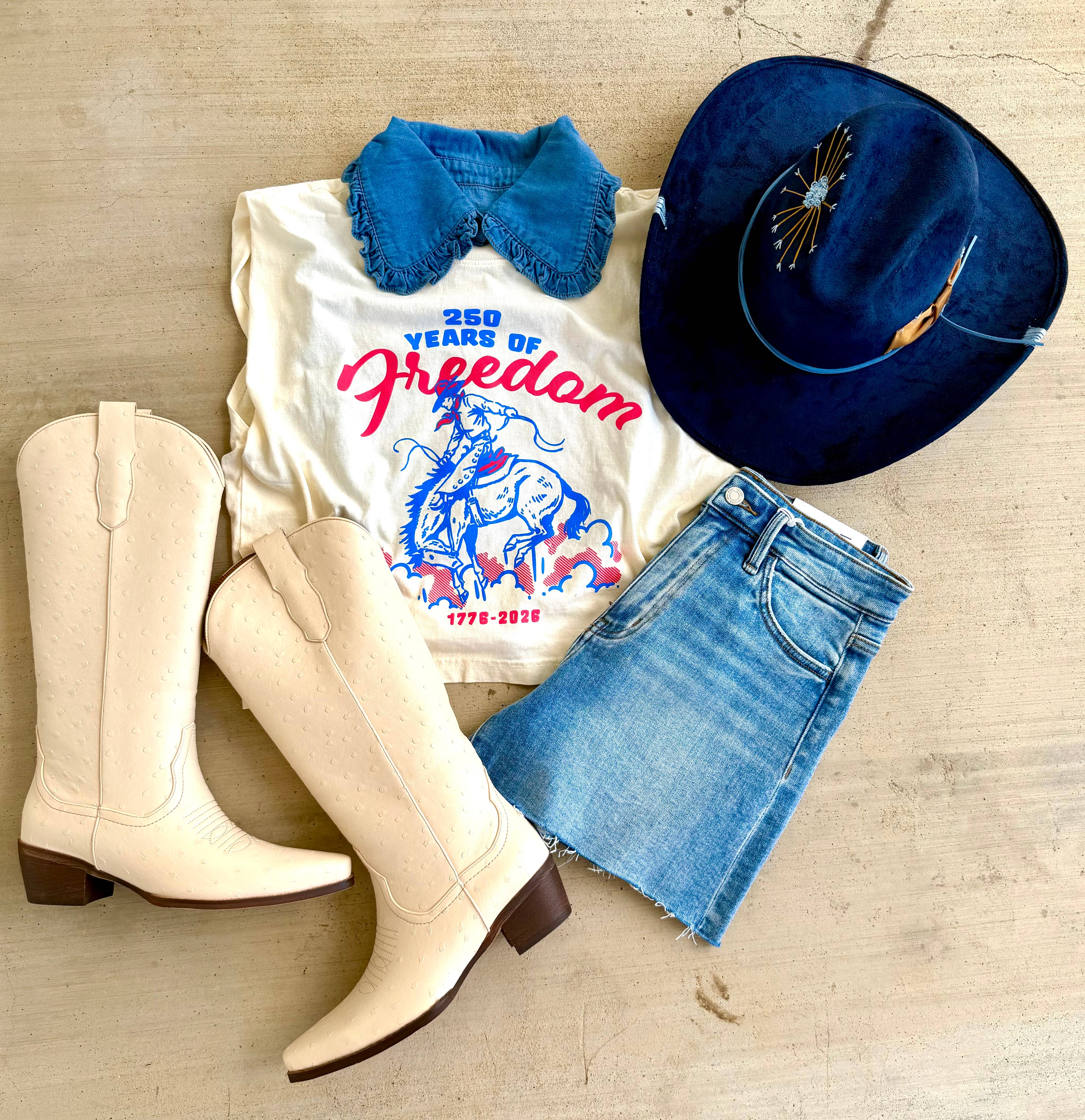 White boots, white t-shirt with graphic design, blue denim shorts, blue hat on a wooden surface