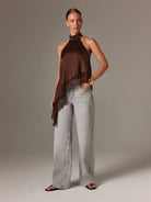 Woman wearing a brown halter top and light gray pants against a neutral background