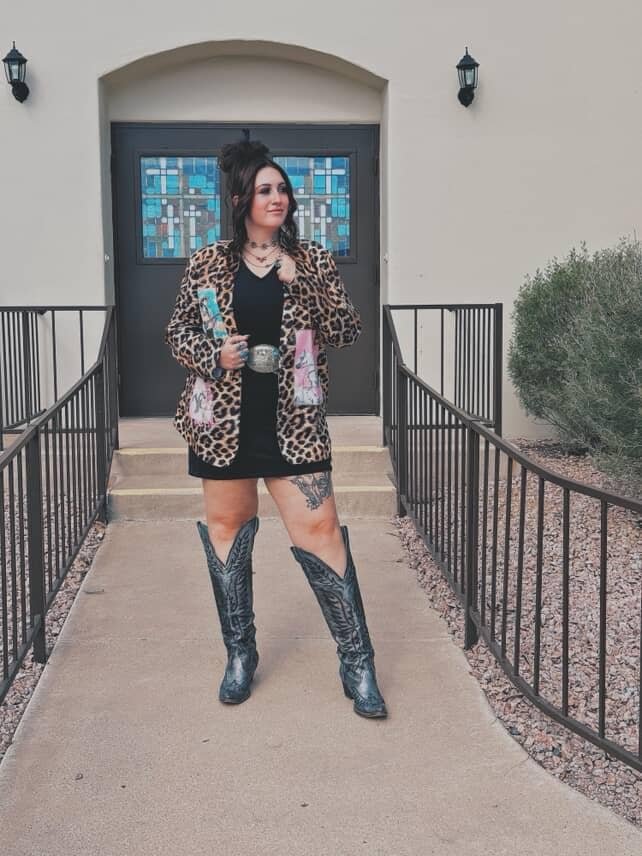 Person wearing a leopard print jacket and black boots standing in front of a building entrance.