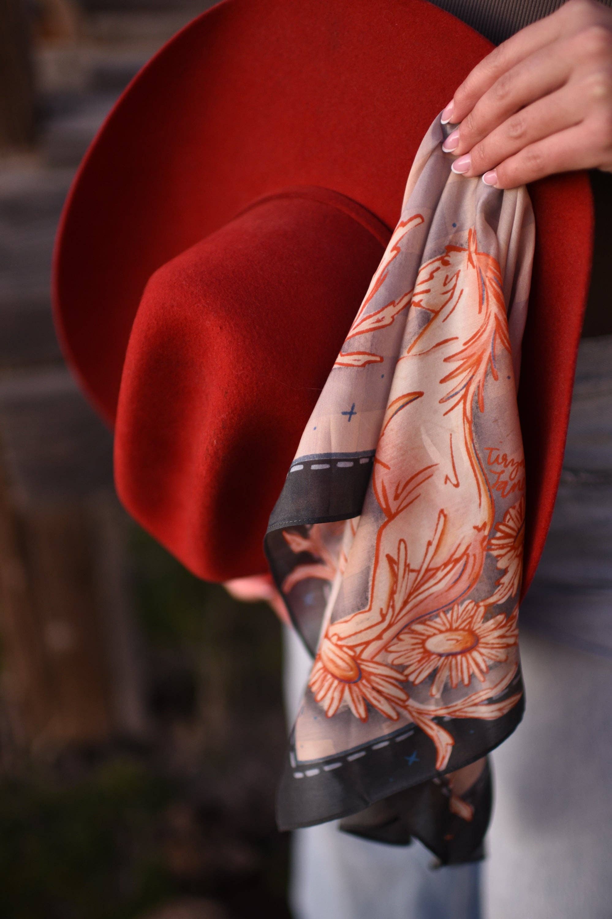 Red hat with a floral patterned scarf held by a hand against a blurred background