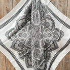Black paisley pattern on a white fabric square against a wooden background