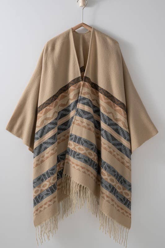 Woman wearing a beige poncho with a  Tan background and light blue, brown, light rust, and grey aztec pattern design  in stripes with tassel trim along bottom hem. Light weight fabric 