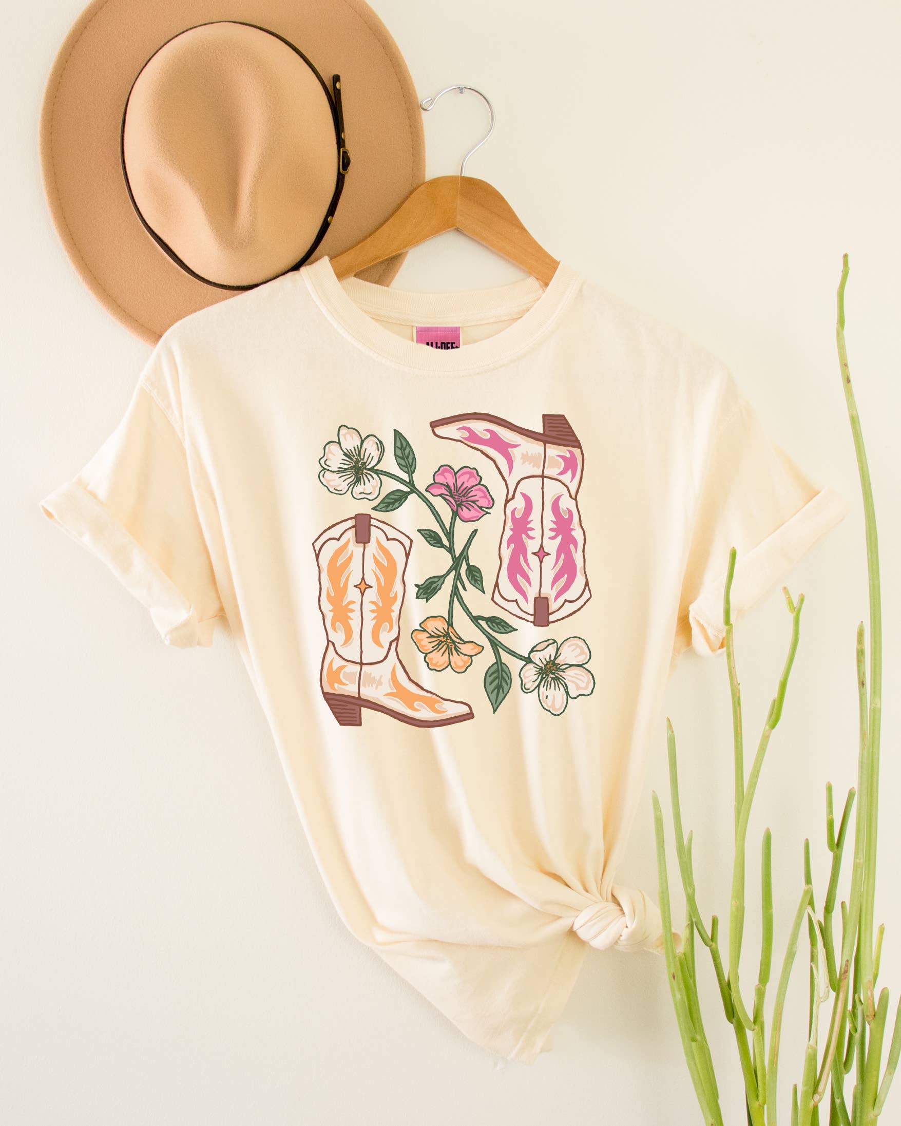 Beige t-shirt with cowboy boot and flower design, beige hat, on a light background