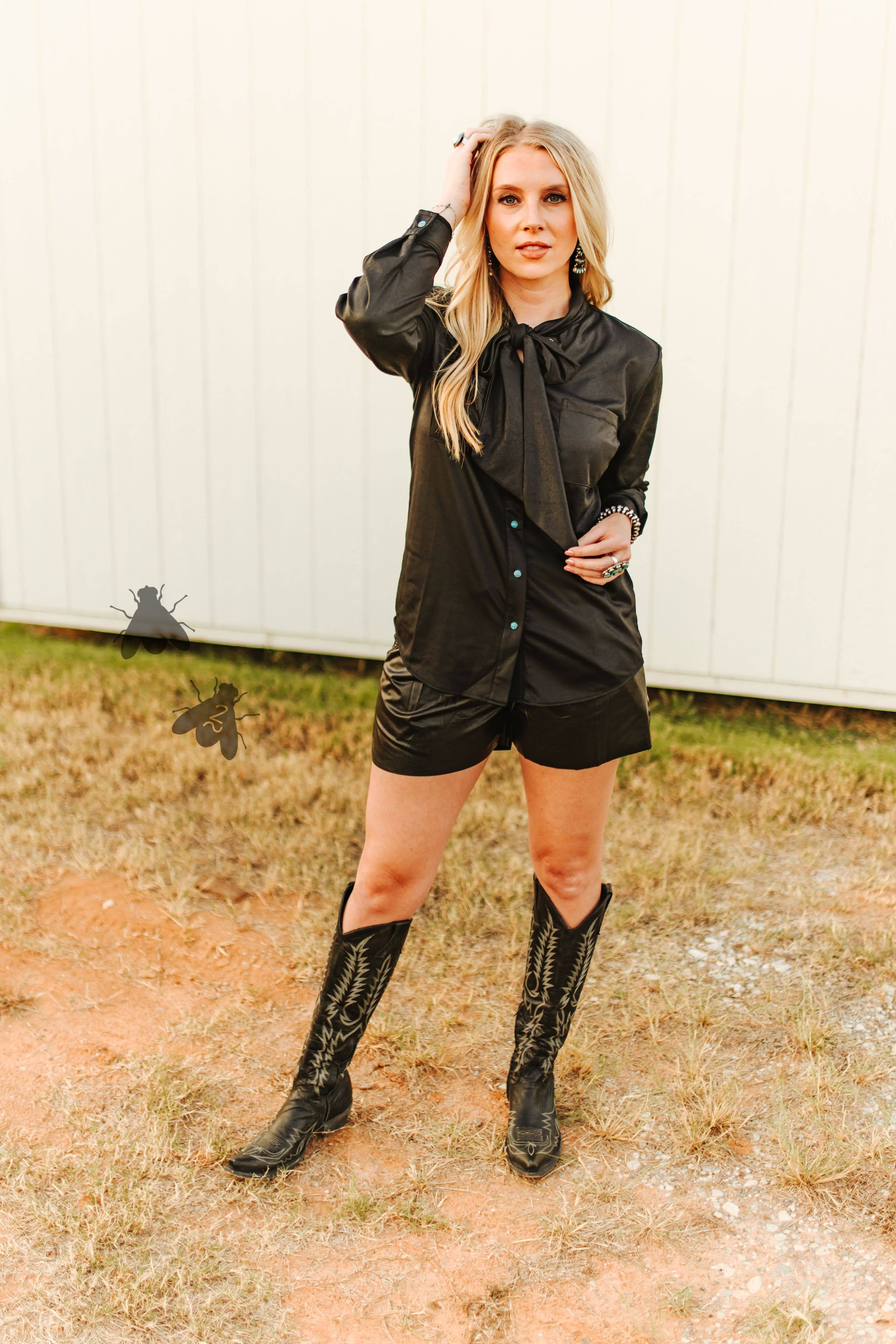 Woman in a black outfit with knee-high boots standing outdoors.