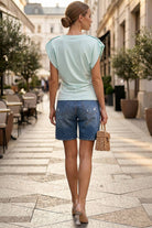 Woman walking on a city street wearing a light blue top and denim shorts.