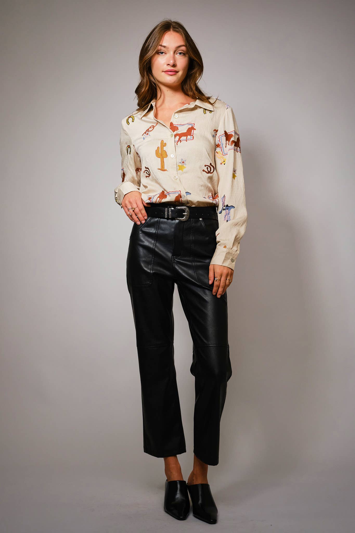 Woman wearing a western embroidery patterned blouse and black pants against a plain background