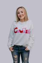 Woman wearing a white sweatshirt with colorful text"COWGIRL" on a plain background